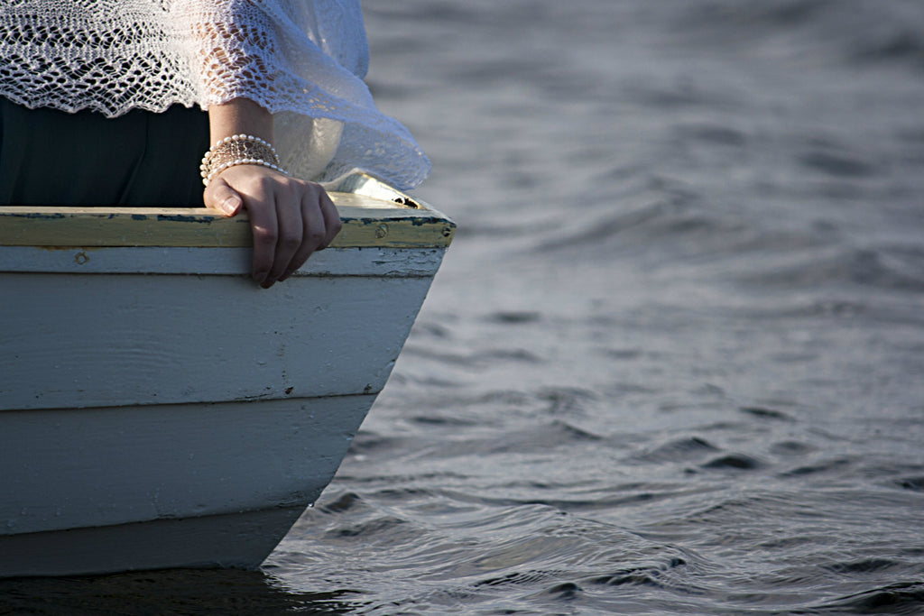 Wooden painted boat with hand holding one. Lass is wearing Shetland Lace Cuff and Hand Knit Shetland Lace Shawl.Boat is on the sea.