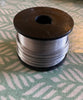 a black reel of silver coloured aluminium wire sits on a tablecloth with a green and white print.